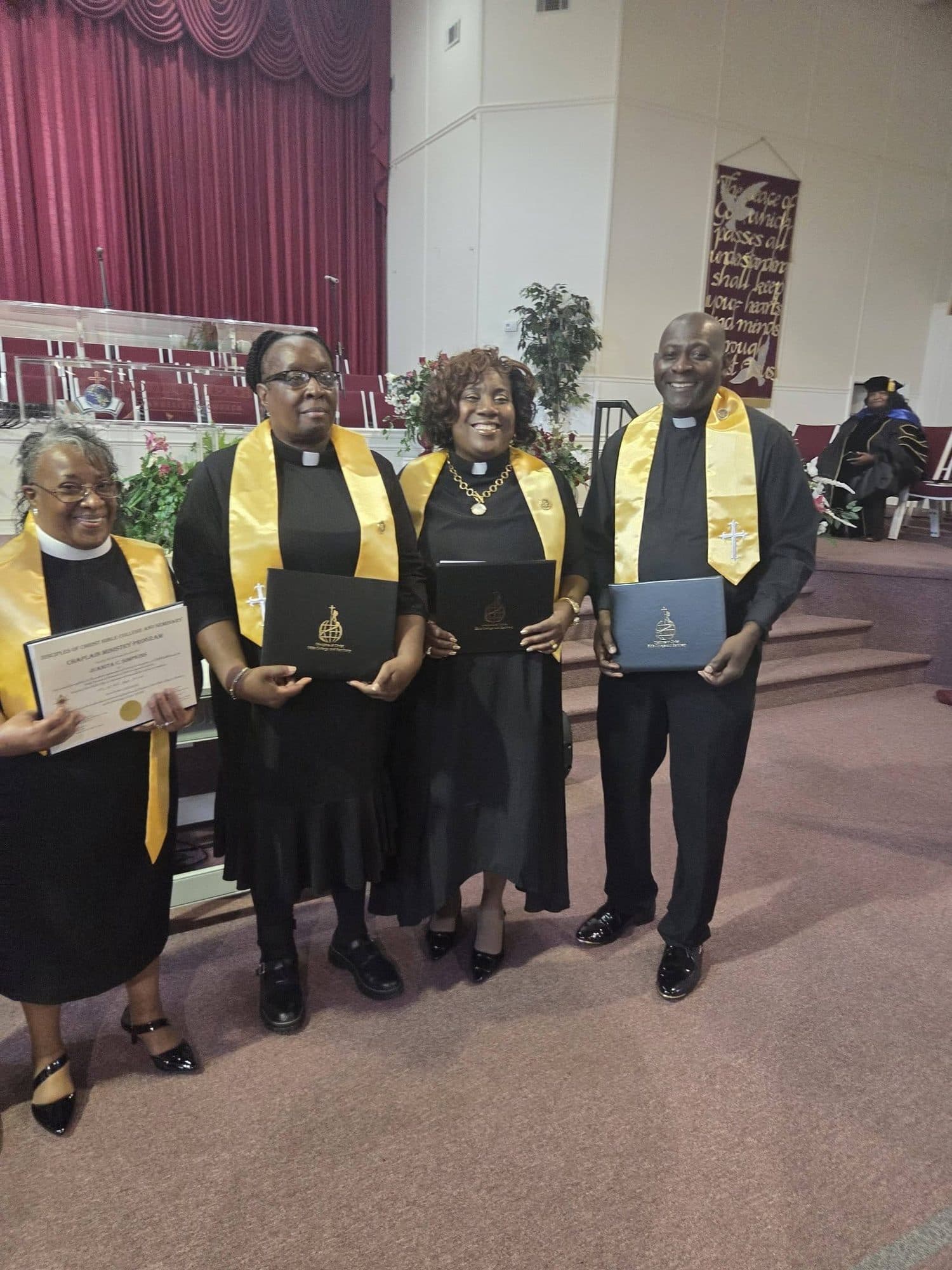 Four new chaplains in clerical collars and gold stoles, smiling and holding their diploma covers