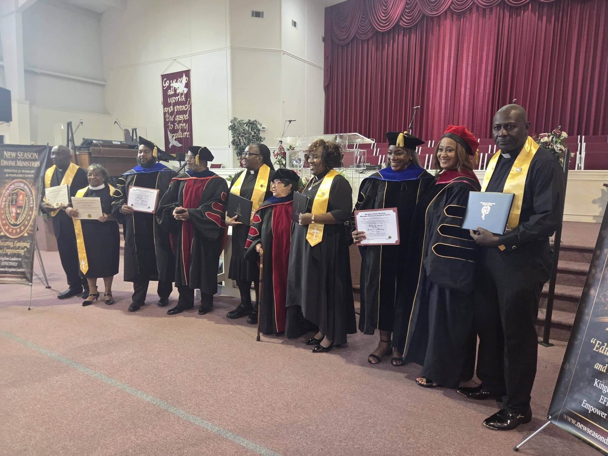 A line of new graduates and faculty in robes holding certificates, beside a New Season Divine Ministries banner reading “Educating, Equipping and Empowering”
